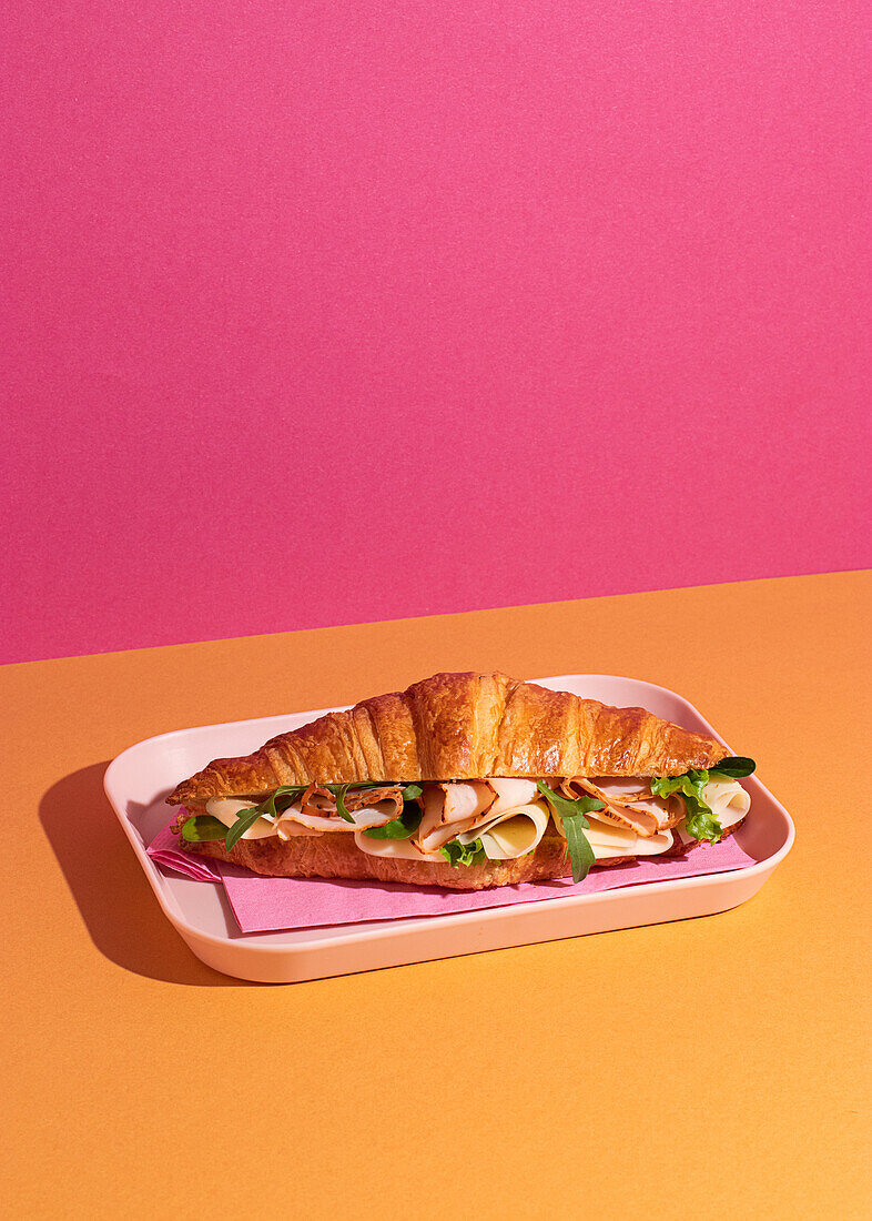 Delicious croissant with ham, cheese and rocket on a plate with a colourful background from above