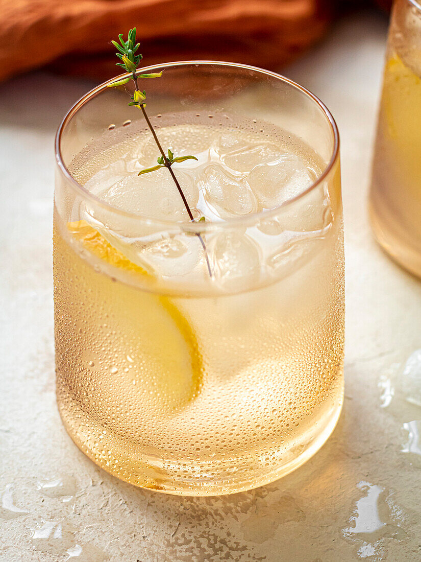Glas Wasser mit Eiswürfeln, dekoriert mit einer Zitronenscheibe und Thymian