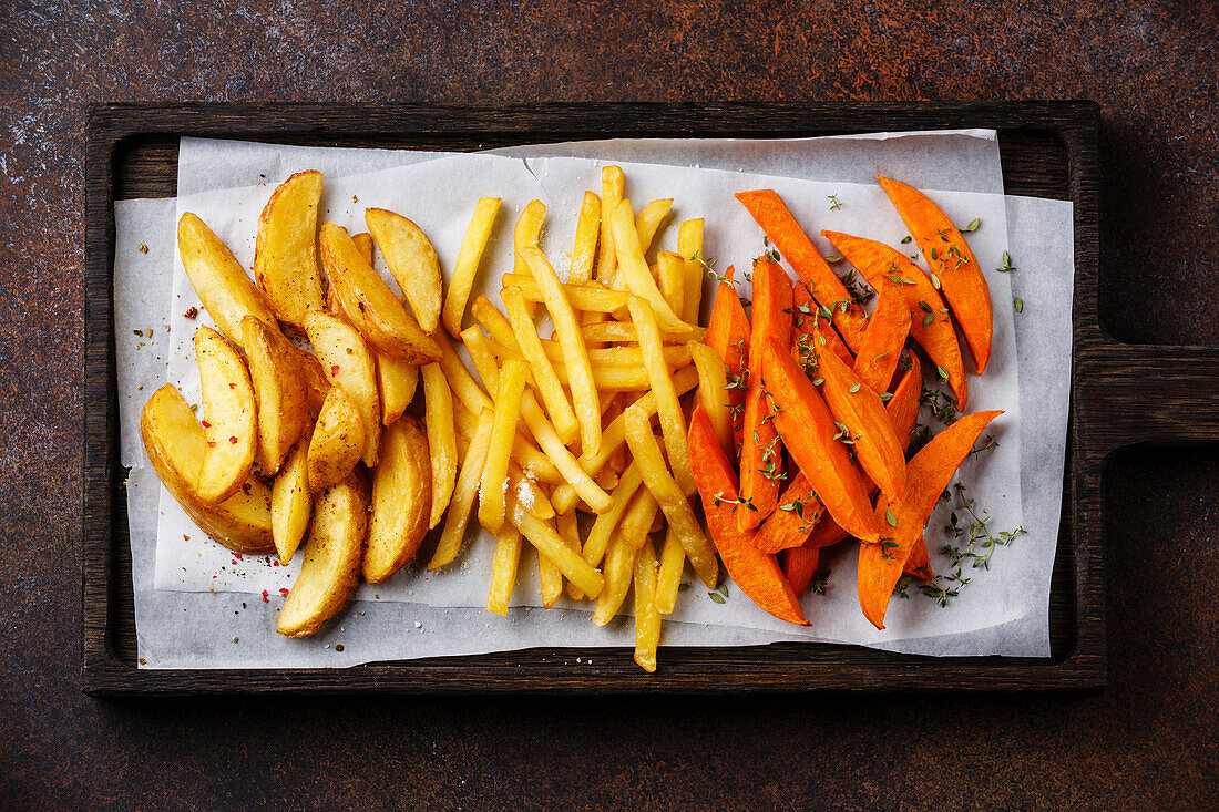 Various potatoes to garnish: Potato wedges, French fries, sweet potatoes on brown background