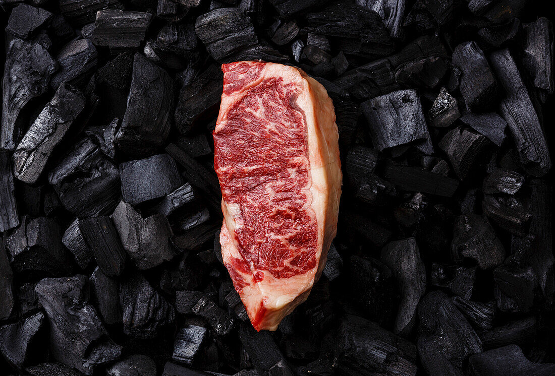 Rohes Frischfleisch Striploin-Steak auf schwarzem Holzkohle-Hintergrund