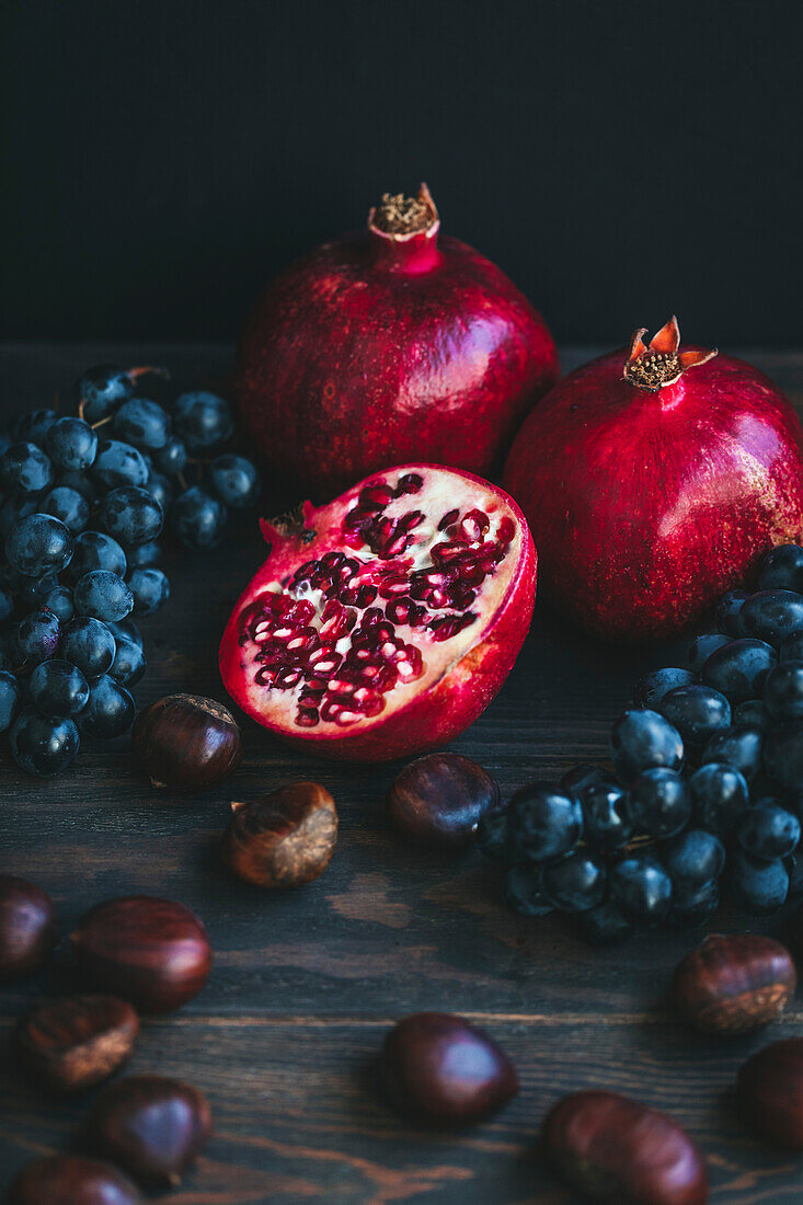 Herbstliche Produkte auf dunklem Hintergrund, darunter Weintrauben, Kastanien und Granatäpfel