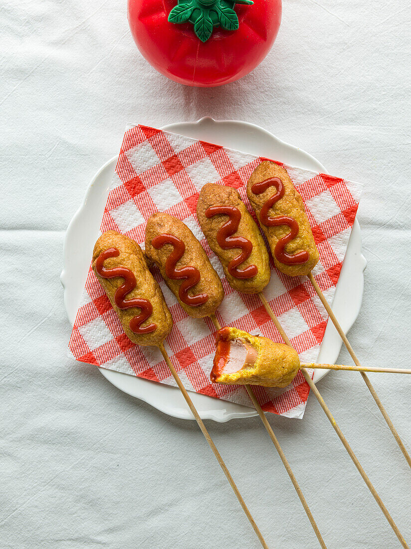 Corn dogs on white plate with checked napkin and tomato sauce.