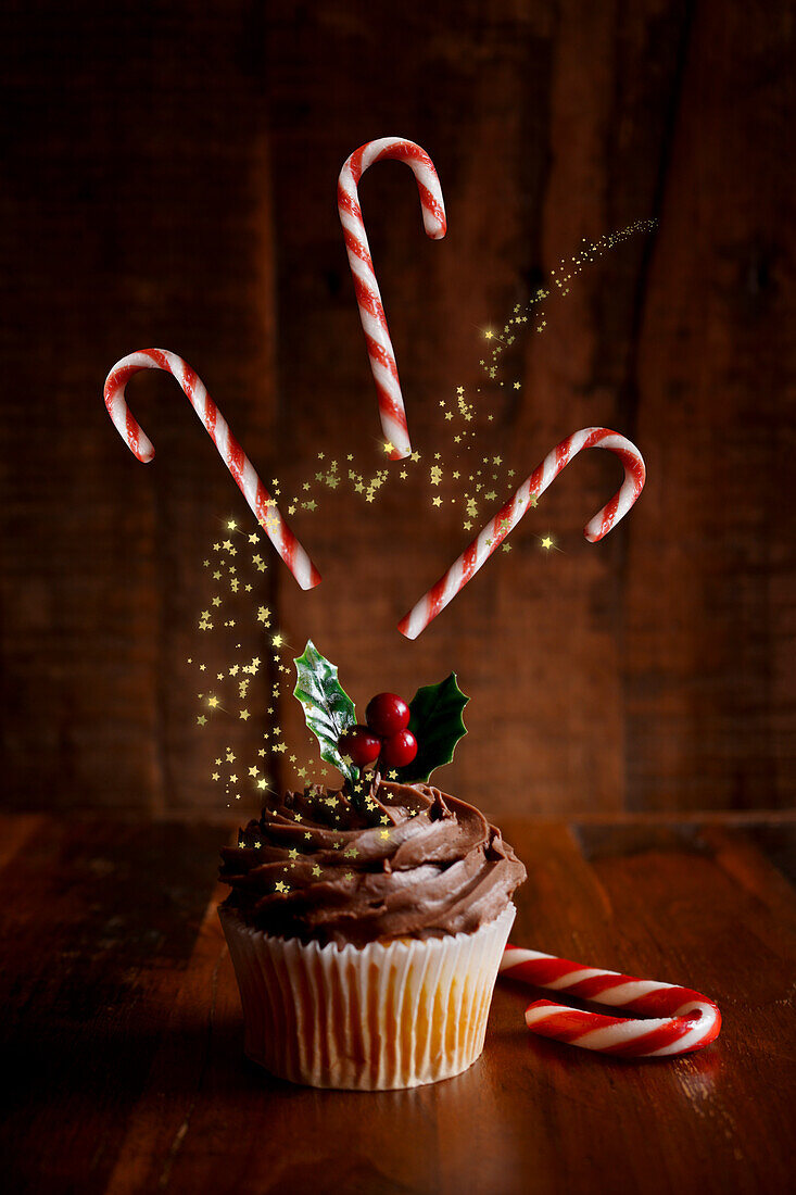 Weihnachtlicher Schokoladen-Cupcake mit fliegenden Zuckerstangen vor einem dunklen Holzhintergrund