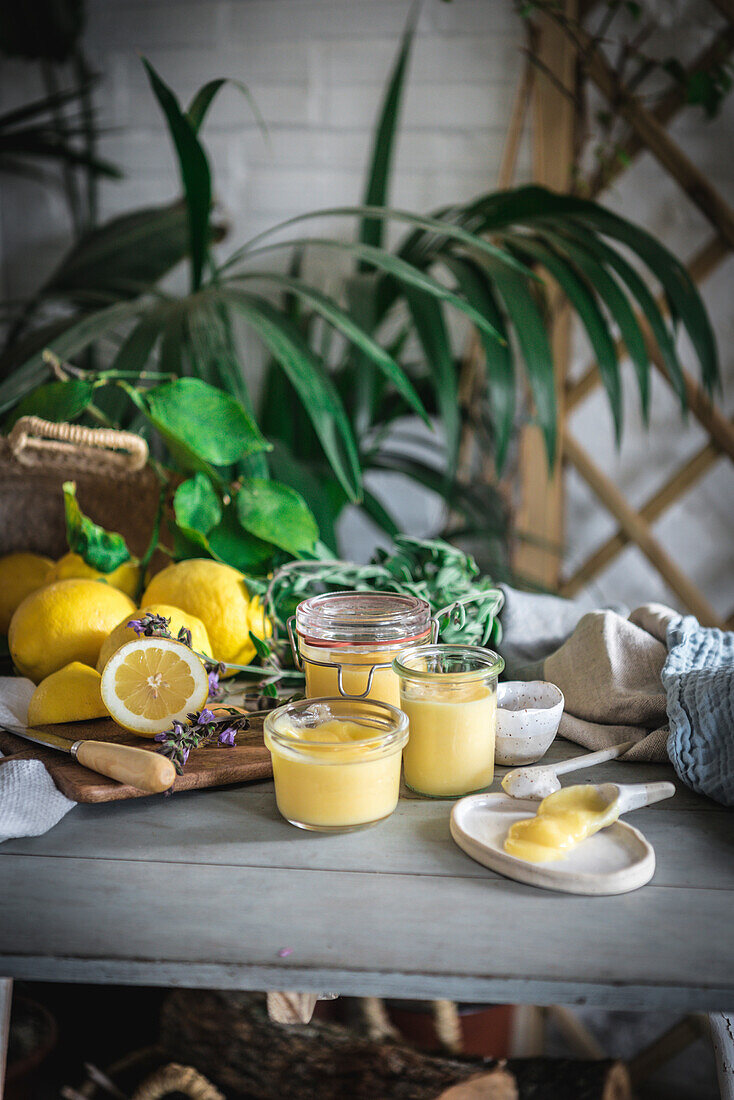 Hausgemachter Lemon Curd in Gläsern, umgeben von Zitronen in einer rustikalen Küche