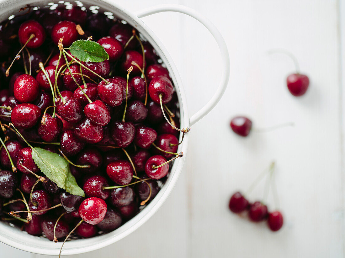 Fresh ripe cherries in white stainless steel colander. Top view of wet red cherry over white woden background. Shallow DOF. Cherries aestetic. Copy space
