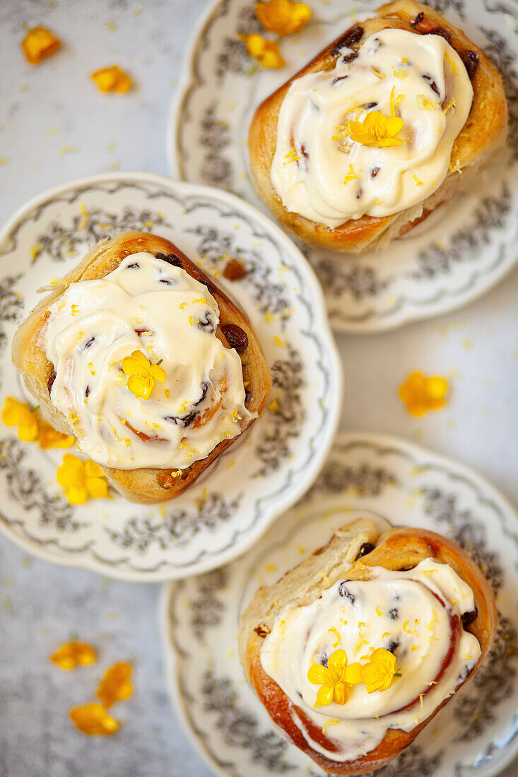 Three lemon rolls topped with cream cheese frosting, presented on plates and garnished with yellow flowers.