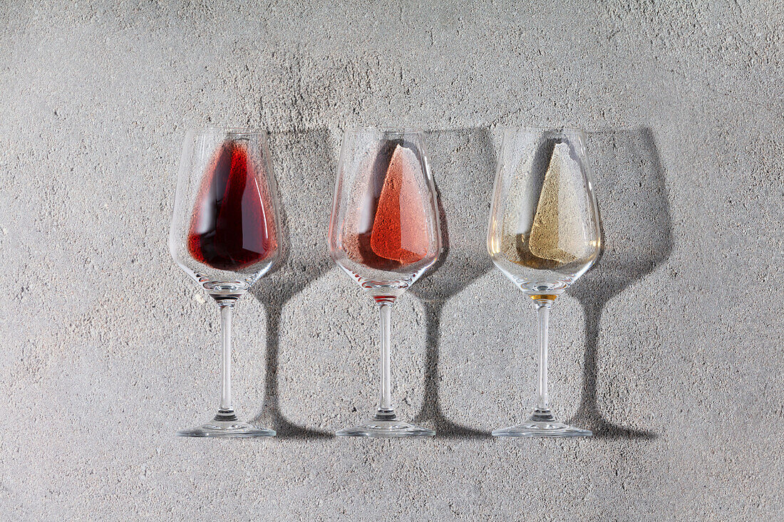 Red, rosé and white wine in glasses on a grey stone background. Wine bar, winery, wine tasting concept. Minimalist trendy photography