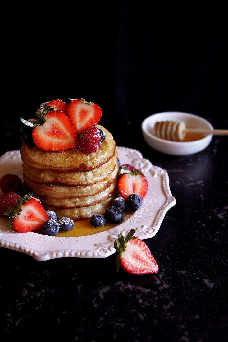 Stack of English style crumpets served with berries and honey.