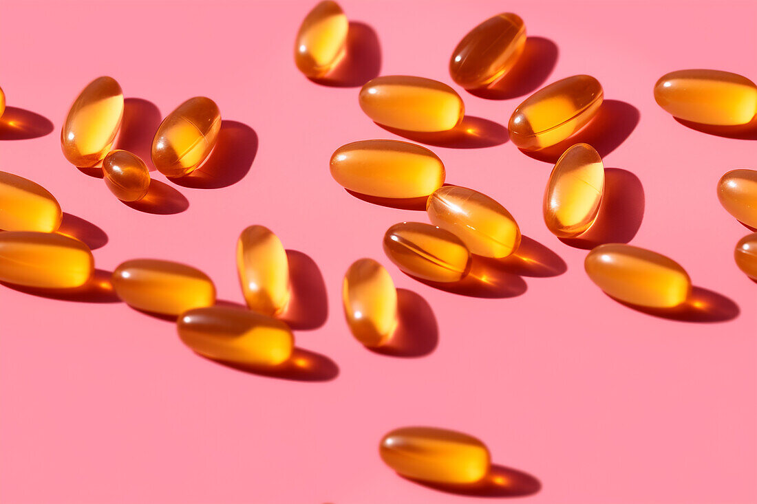 Composition of orange-coloured vitamin pills scattered on a pink background in a bright studio