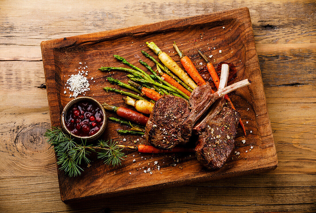 Gegrillte Hirschrippchen mit gebackenem Gemüse und Beerensauce auf Holzuntergrund