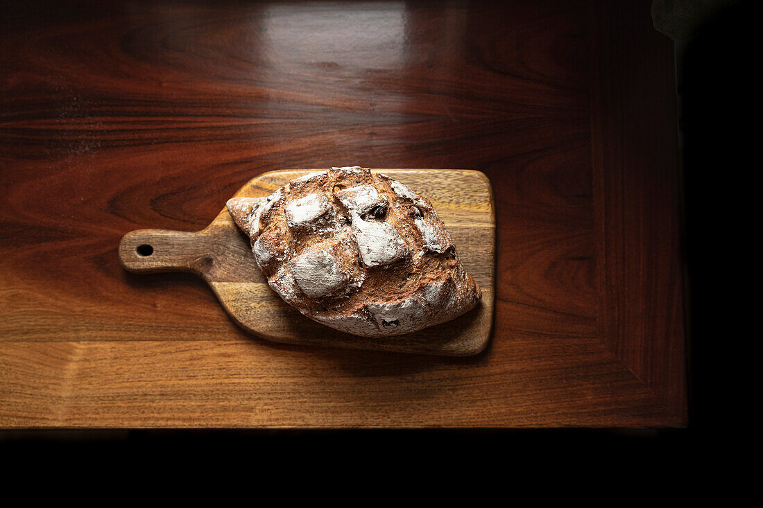Rustic loaf of bread on antique wooden chopping board
