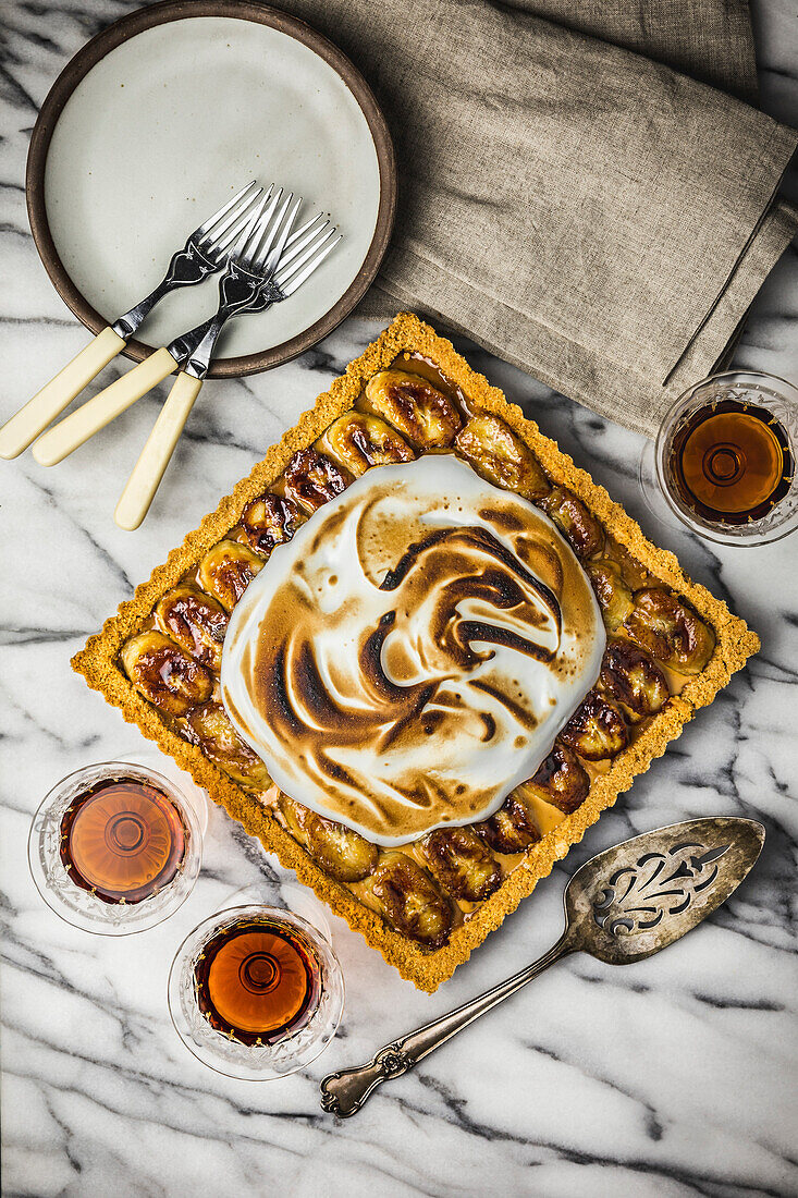 Banana Cream tart with toasted marshmallow topping on marble surface with rum in vintage glasses