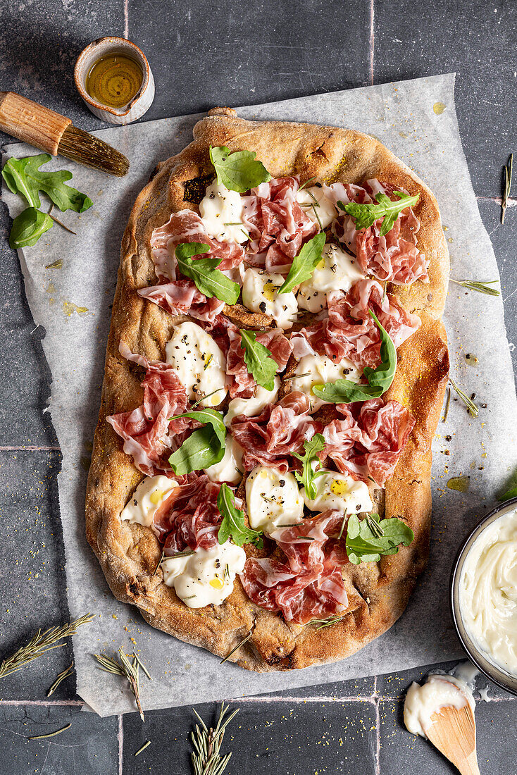 Pizza with cheese, prosciutto, rocket and olive oil