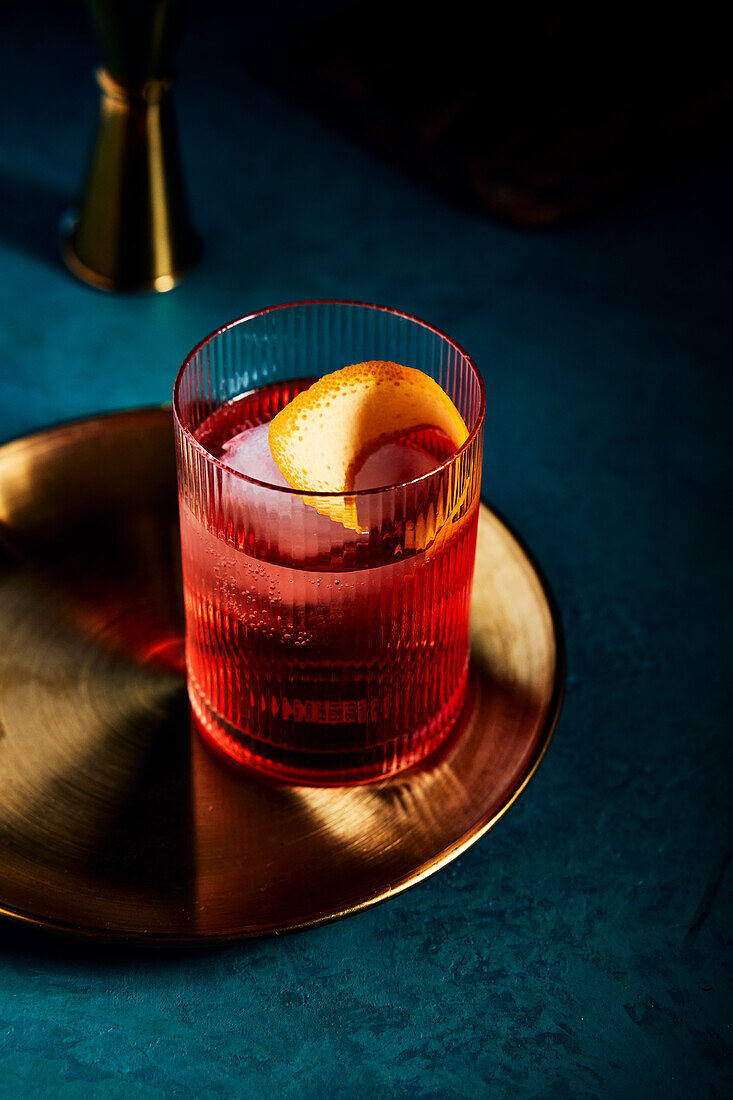 Negroni cocktail on golden tray on blue-green background