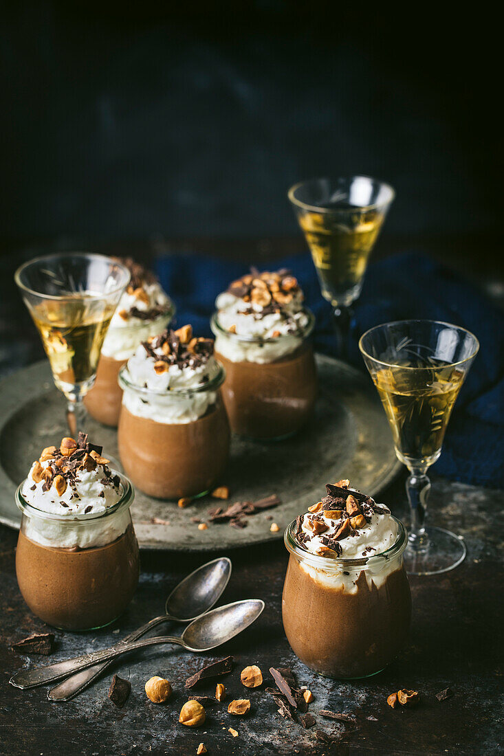 Individual jars of chocolate mousse, topped with whipped cream, hazelnuts and shaved chocolate. Vintage glasses with deesert liqueur