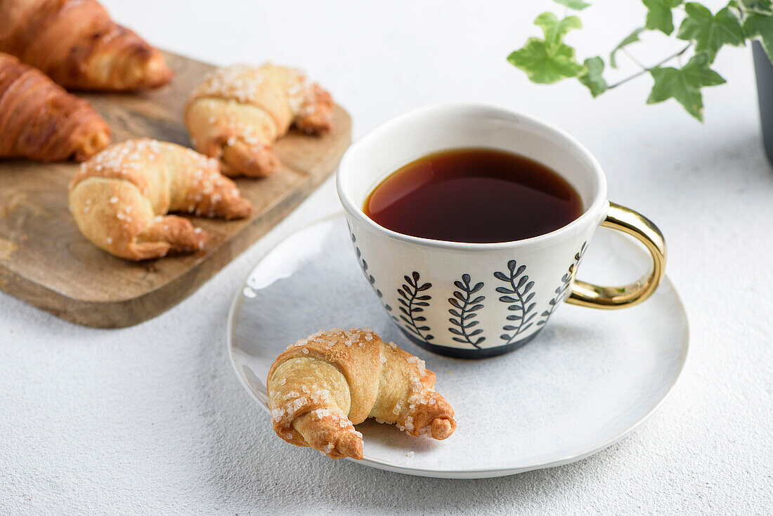 Die Tasse Tee auf einer Untertasse und ein Croissant