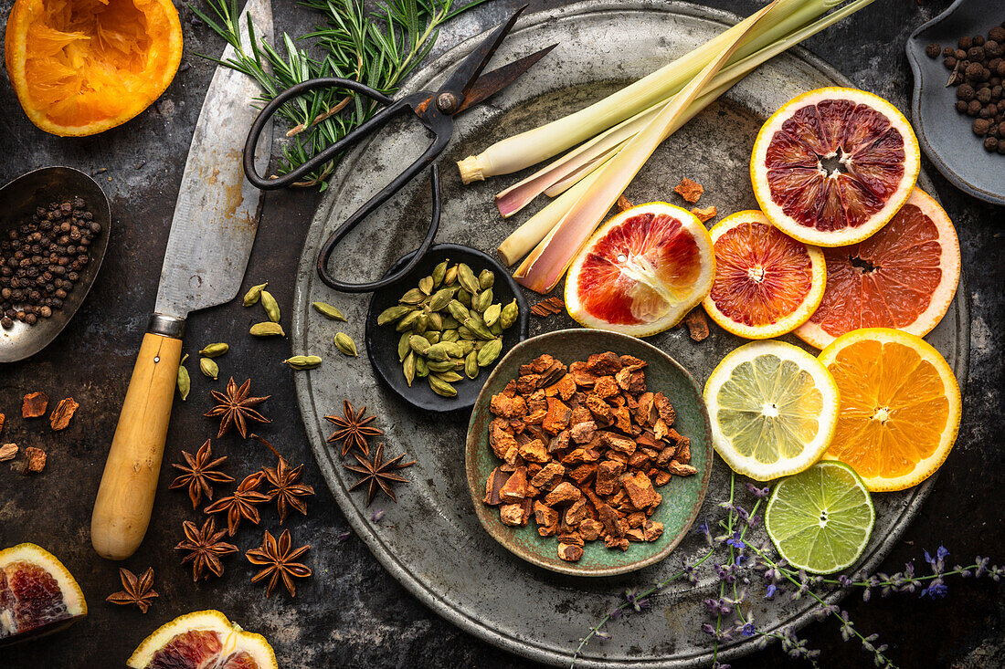 Flat lay arrangement of colourful citrus slices, fruit juices, lemongrass, herbs and spices on a dark background. Ingredients for homemade tonic water for cocktails