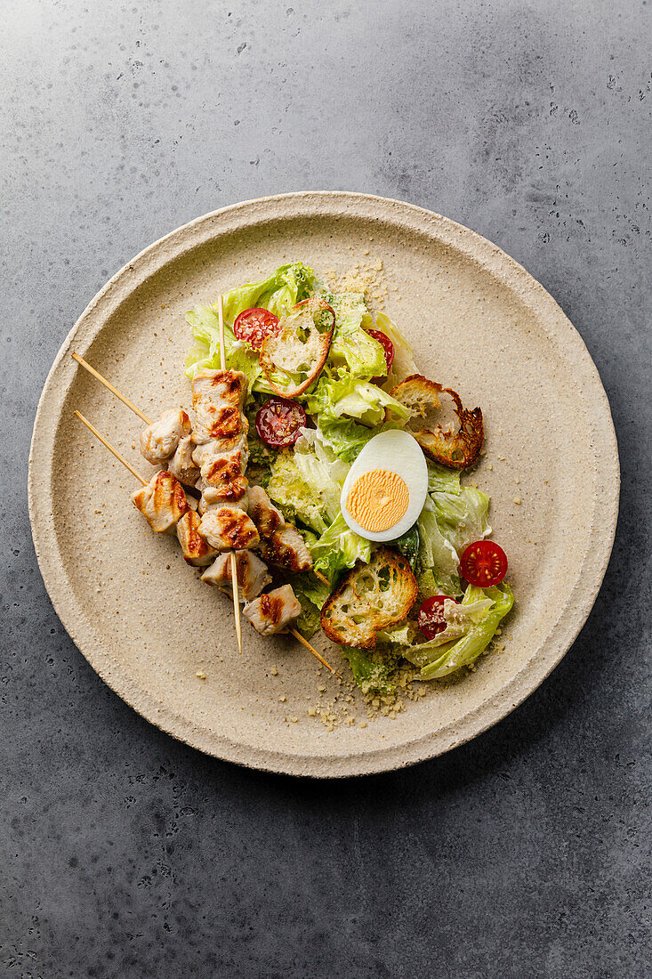 Caesar salad with chicken breast on a skewer and egg on a plate