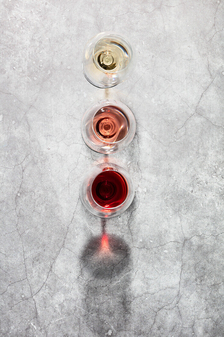 Flat-lay of red, rose and white wine in glasses on grey stone background. Wine bar, winery, wine degustation concept. Minimalistic trendy photography.
