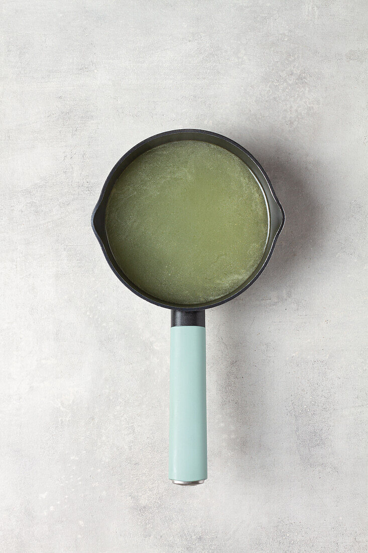 Black pan with blue handle in round shape with green watery broth on grey table seen from above