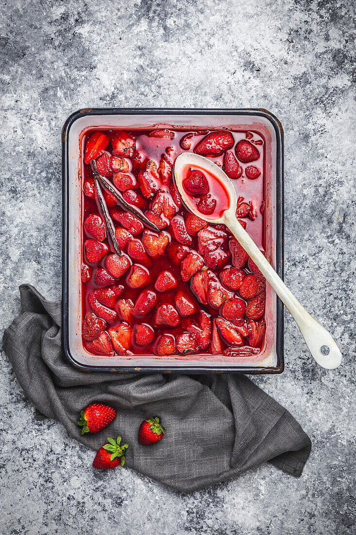Roasted strawberries in an enamelled tray with vanilla pod