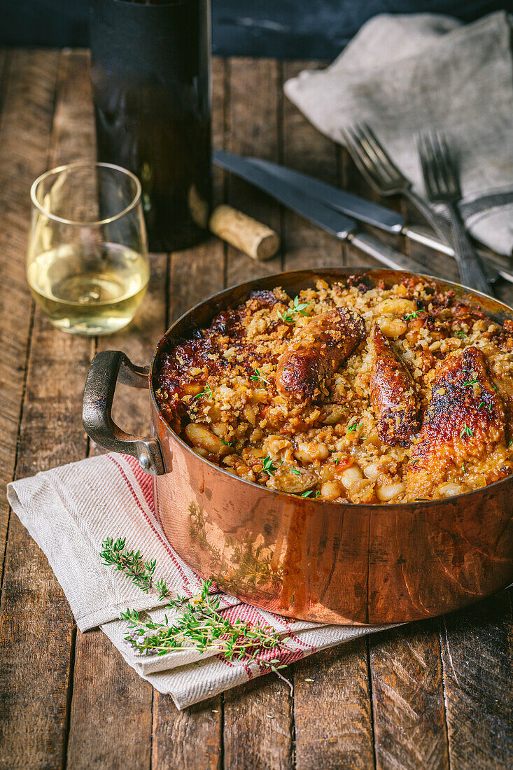Classic French cassoulet with chicken and sausage in antique copper pot with wine glass and bottle