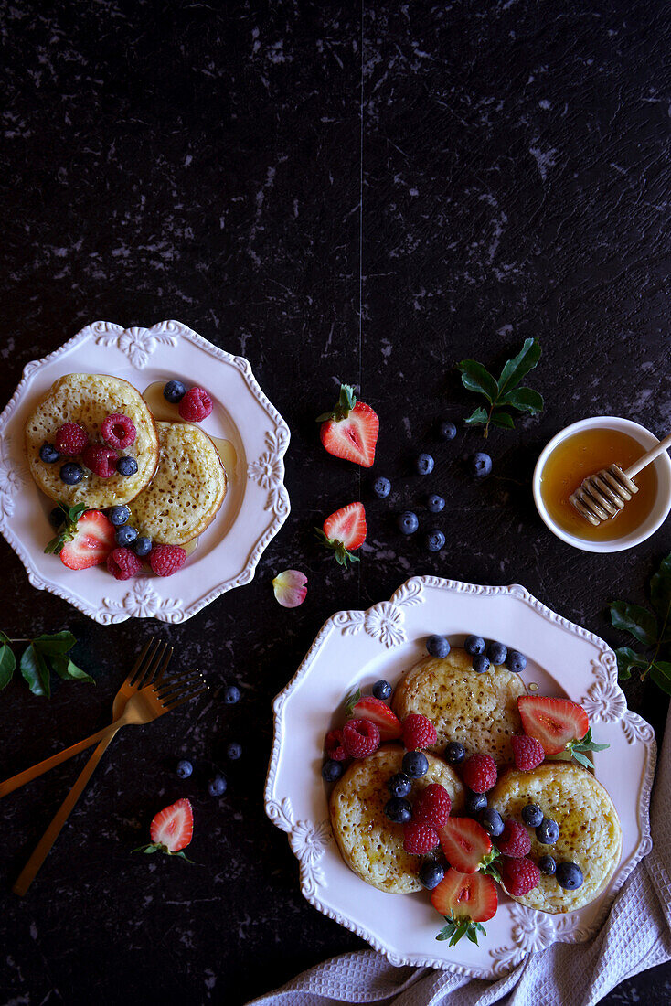 English-style crumpets with berries and honey on a black marble background, flatlay with copy template