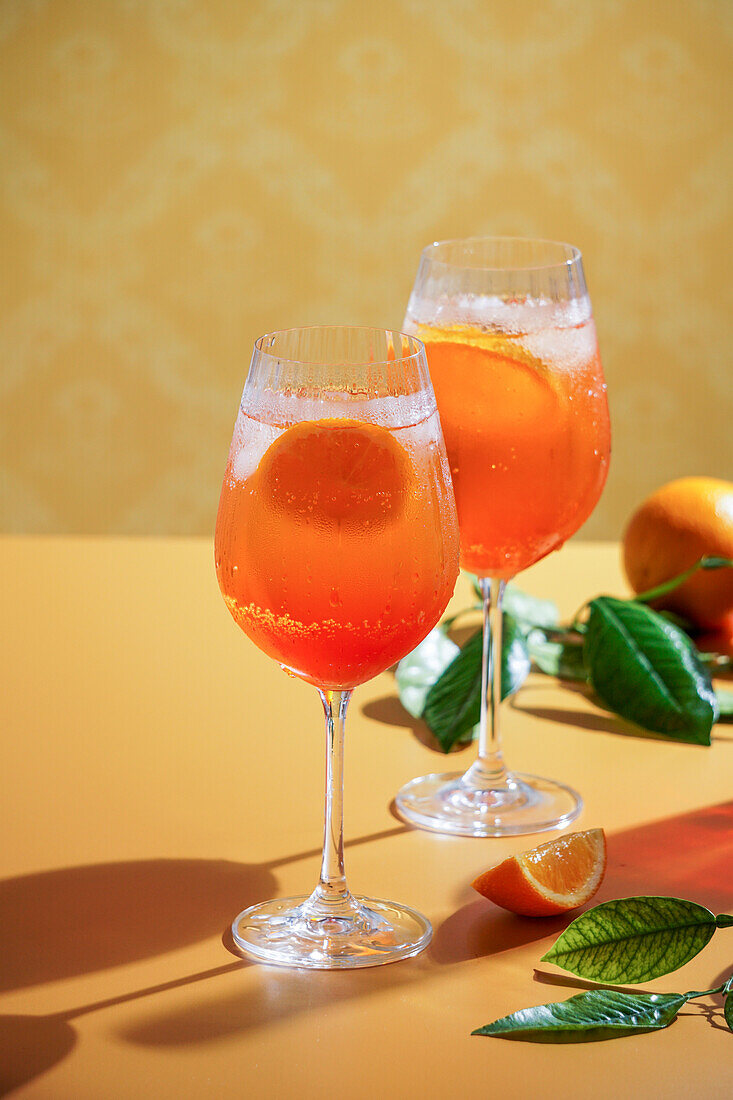 Aperol Spritz Cocktail mit Eis, ein beschlagenes erfrischendes Getränk, auf einem orangefarbenen Hintergrund, Sonnenlicht, Schatten, ein Sommergetränk in einem Weinglas