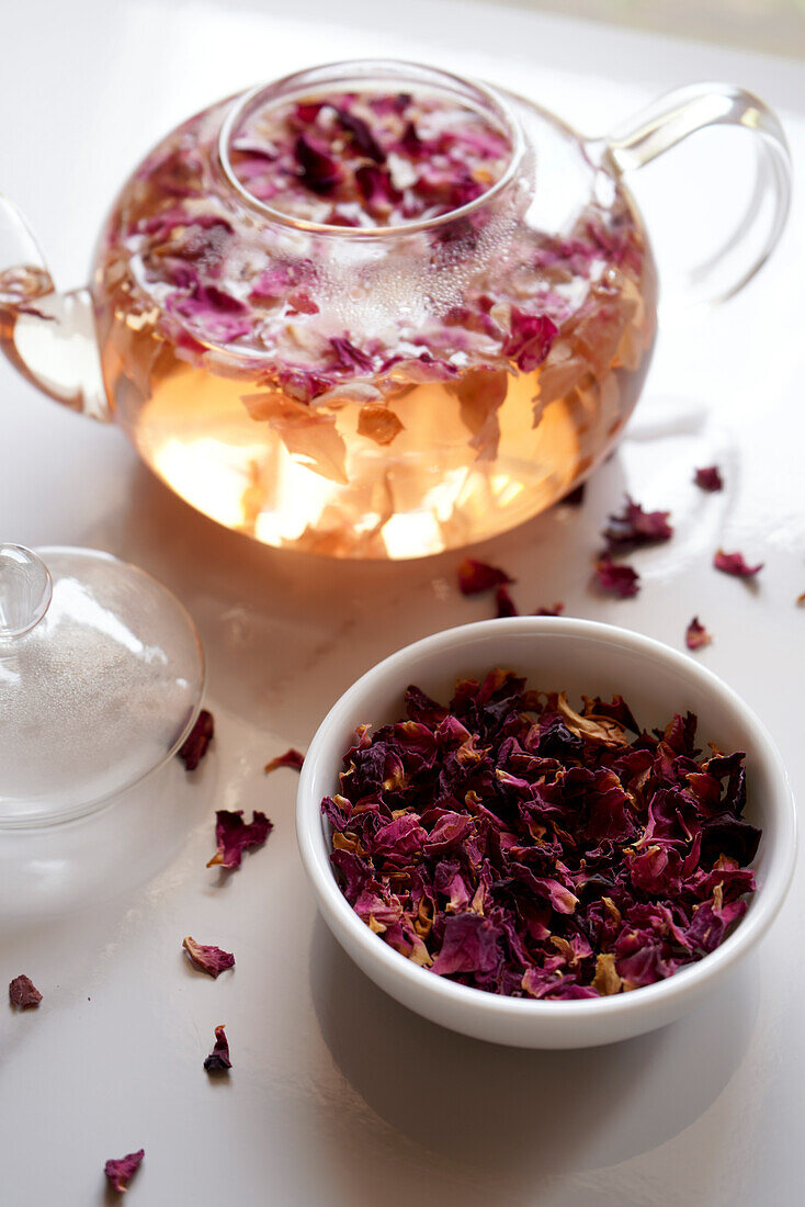 Rose petal herbal tea with dried flowers and teapot closeup.