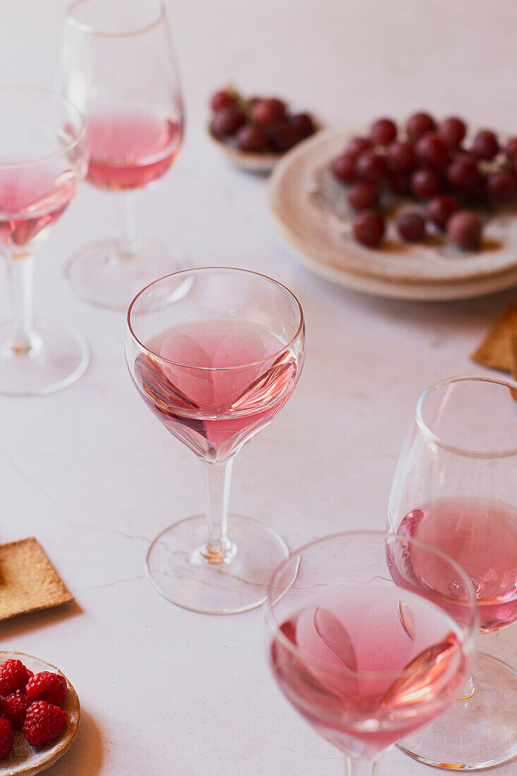 Gläser mit rosafarbenem Wein und Weintrauben im Hintergrund