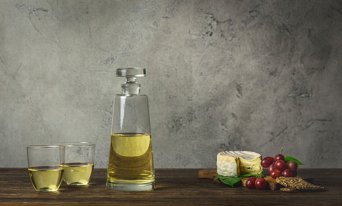 White wine in stemless glasses and modern carafe with Brie cheese and grapes