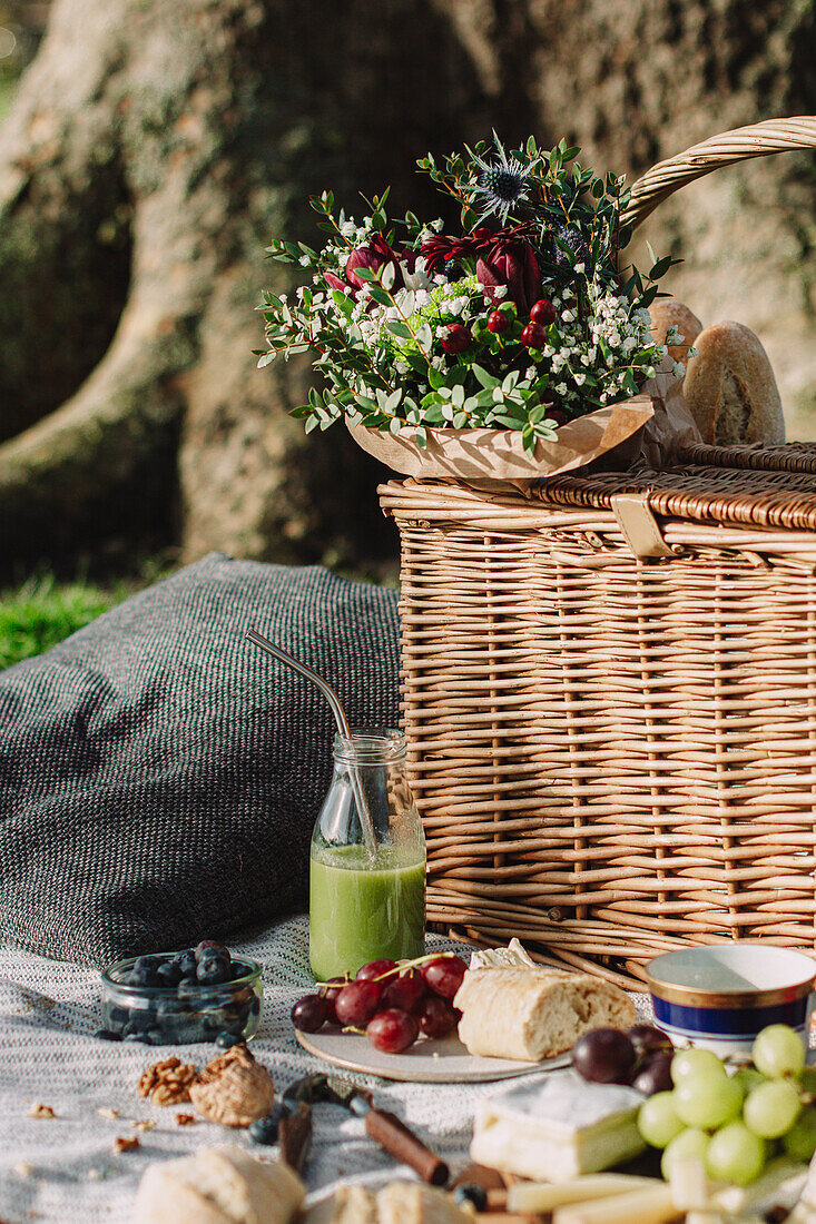 Picnic scene with a basket and flowers, green juice and plate with grapes, cheese and baguette Juice and plate with grapes, cheese and baguette