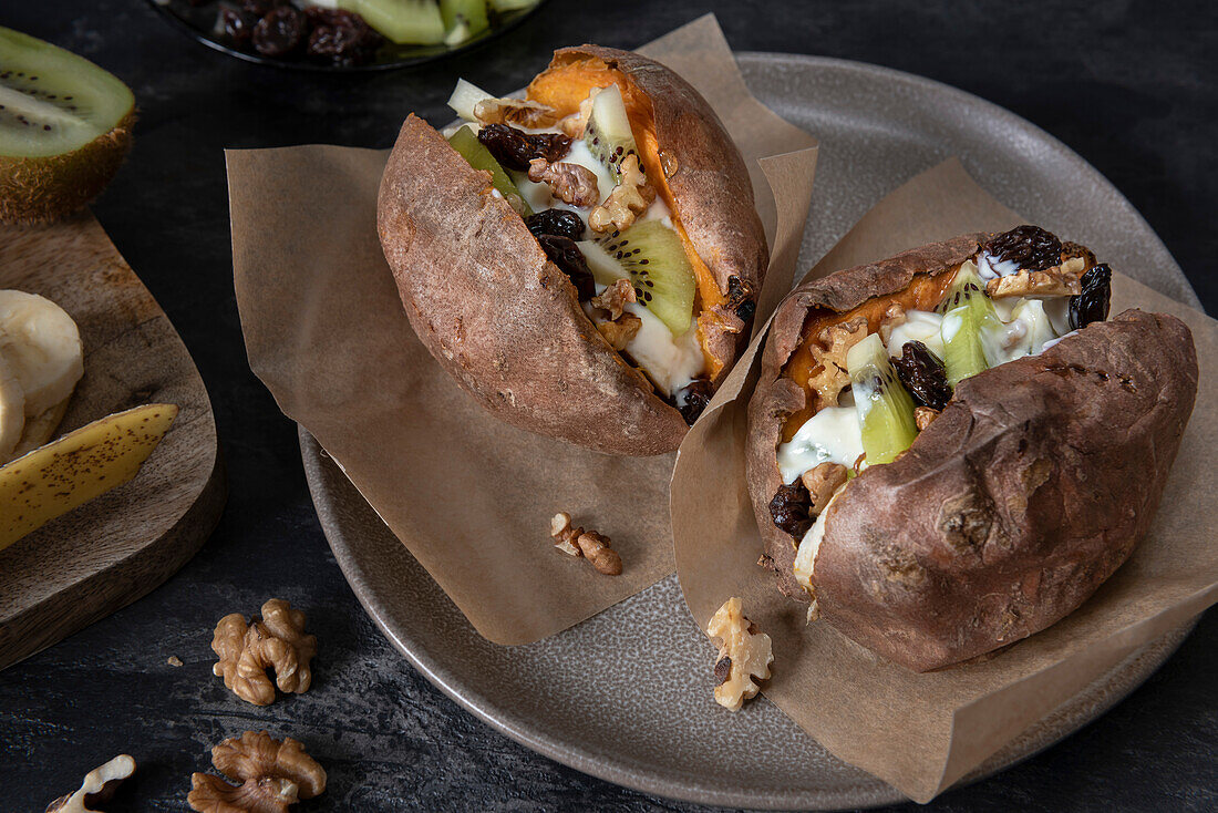 Baked sweet potato with fruit. The dish consists of sweet potato, banana, kiwi, sultanas, walnuts and coconut yoghurt. View from above