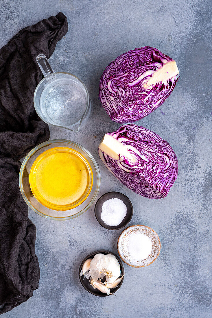 Red cabbage quarters, vinegar, water, garlic, salt and sugar photographed against a grey background