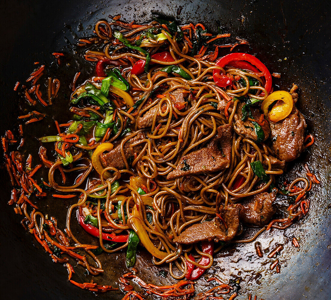 Stir-fried soba noodles with beef and vegetables in a wok pan on a dark background Close-up
