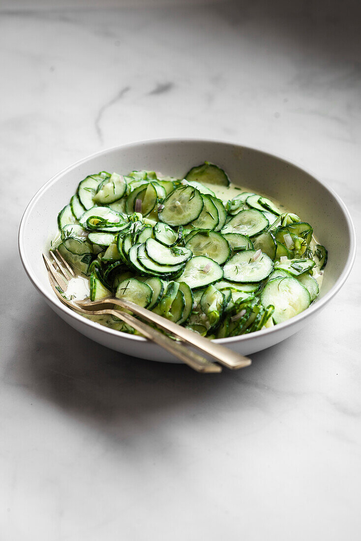 A bowl of German cucumber salad on a marble table