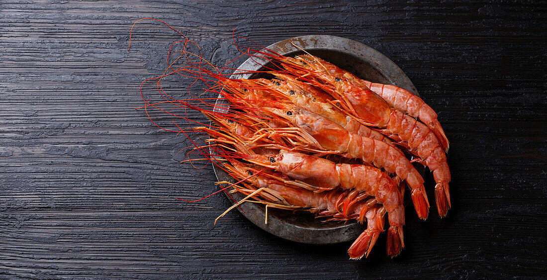 Raw fresh prawn on metal plate on black burnt wood background Copy space