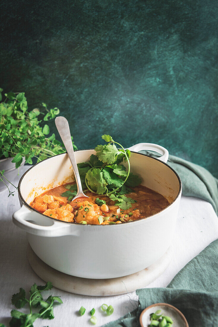 Cauliflower and chickpea curry in a large pan, served with herbs