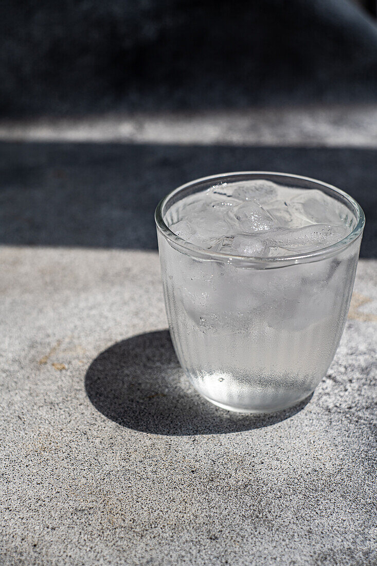 Glas reines Wasser mit Eiswürfeln in heißem Sommertag auf Betontisch Hintergrund
