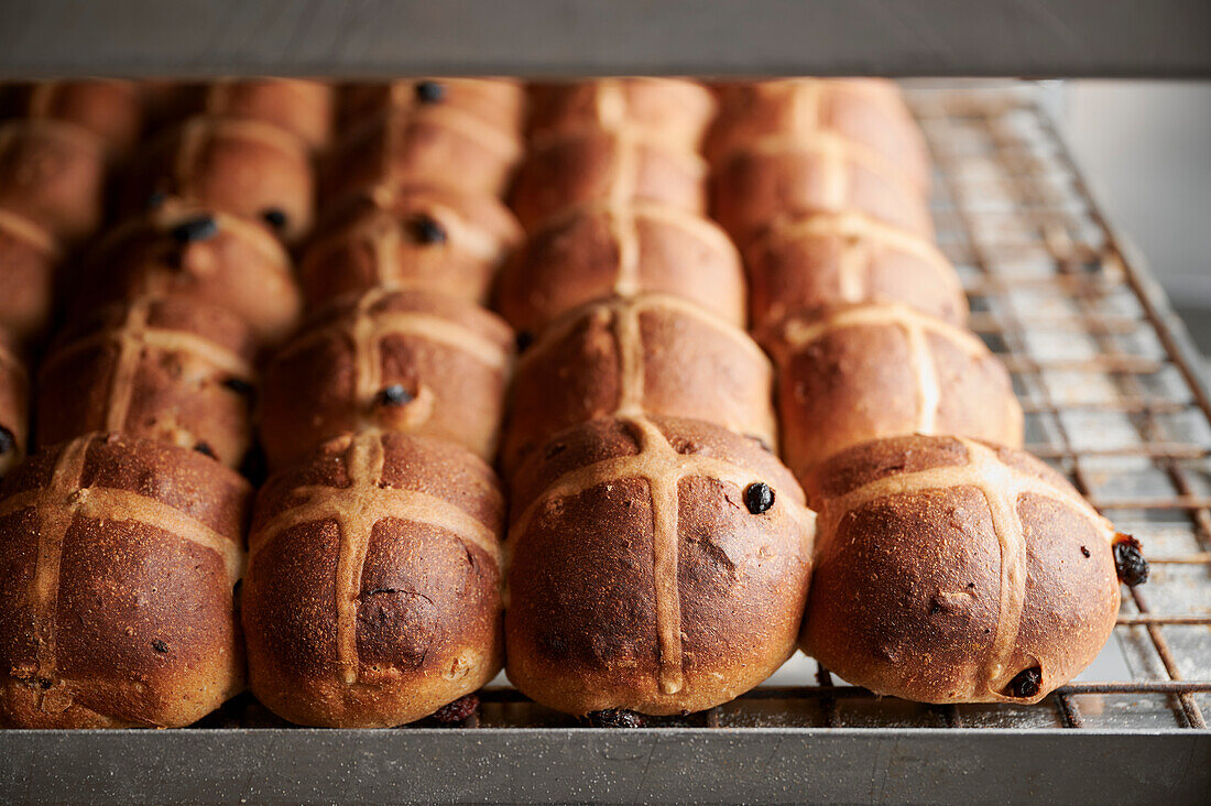 Freshly baked fruit hot cross buns made with yeast and sourdough cooling on a rack on a bakery trolley