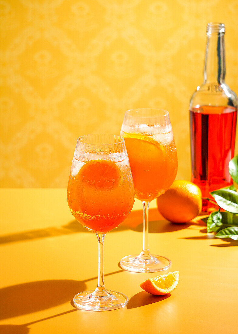 Aperol Spritz Cocktail mit Eis, ein beschlagenes erfrischendes Getränk, auf einem orangefarbenen Hintergrund, Sonnenlicht, Schatten, ein Sommergetränk in einem Weinglas