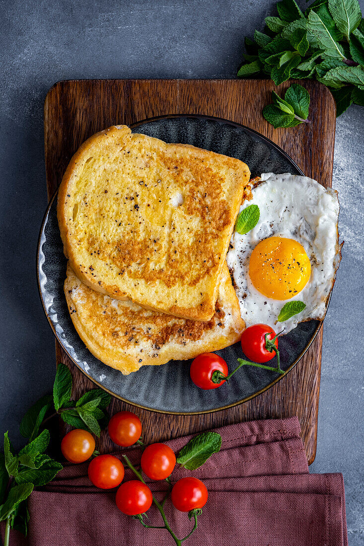 A breakfast plate loaded with French toast slices and a fried egg garnished with fresh mint leaves and cherry tomatoes.