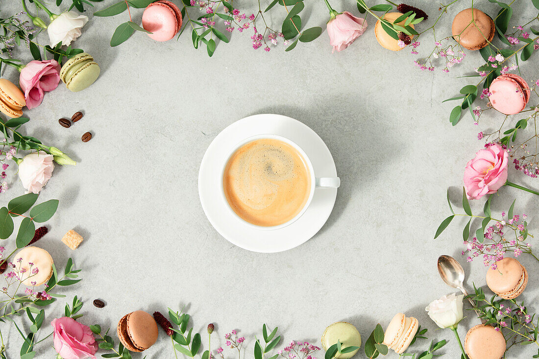 Weiße Tasse Kaffee und Rahmen aus Frühlingsblumen und verschiedenen Makronensorten flach gelegt