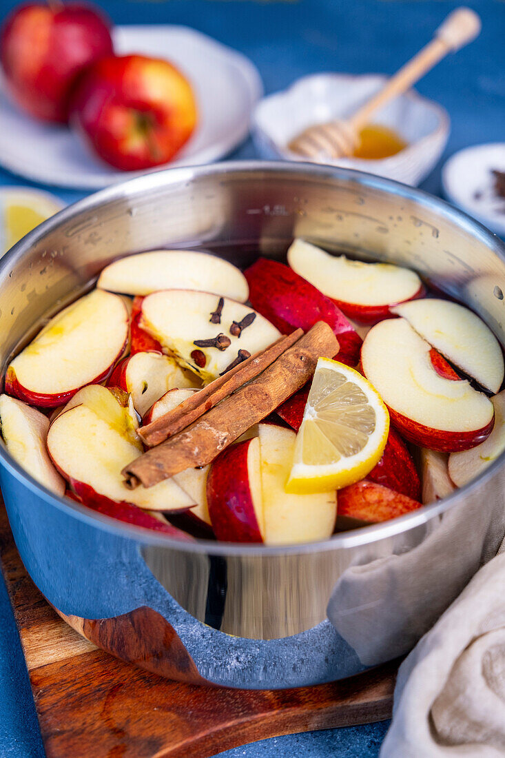 Apple slices ready to be cooked in water with a cinnamon stick and cloves in a saucepan.