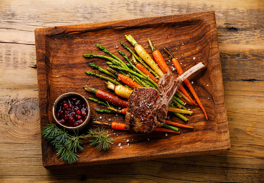 Grilled Venison Ribs with baked vegetables and berry sauce on wooden background