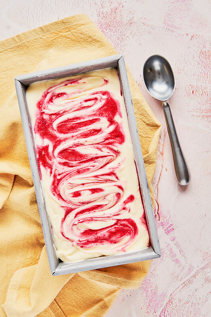 Raspberry Ripple Ice Cream Tub auf rosa Hintergrund mit gelber Serviette