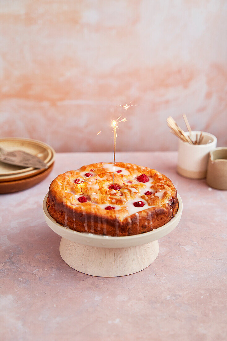 Raspberry ricotta cake with icing on a stand and sparkler