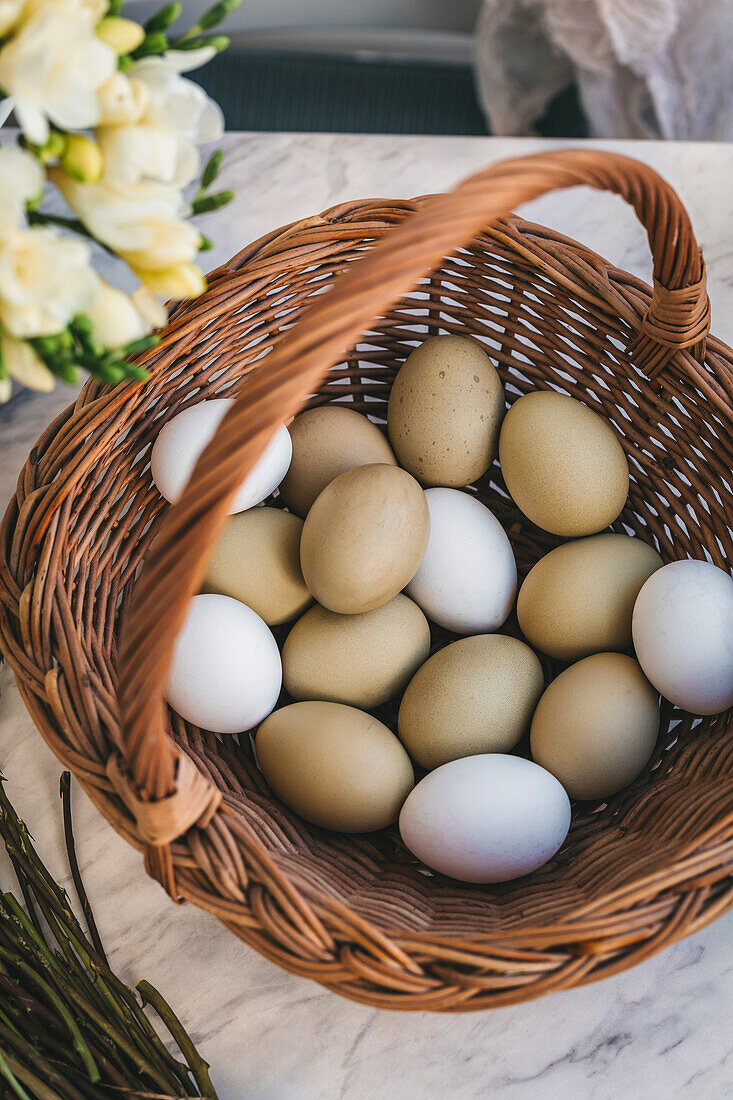 Grüne Eier in einem Weidenkorb auf einem weißen Marmortisch