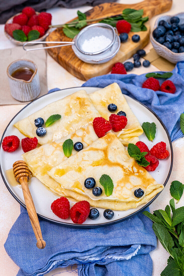 Almond milk crepes garnished with fresh berries and mint leaves on a round plate