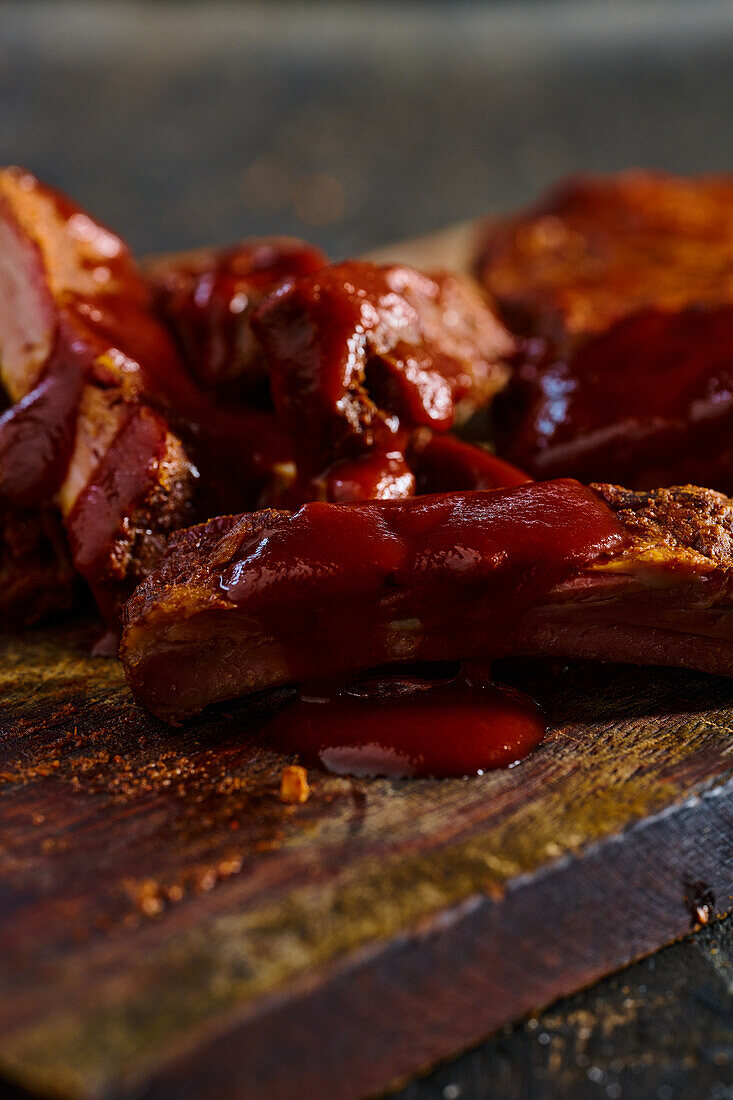 High angle of appetizing grilled pork ribs with barbecue served on wooden board in kitchen against blurred background